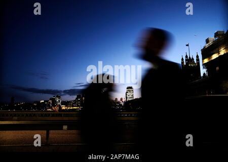 Commuters pedestrians walkers at dusk as shadows passing each other crossing Westminster Bridge London Houses of Parliament background Stock Photo