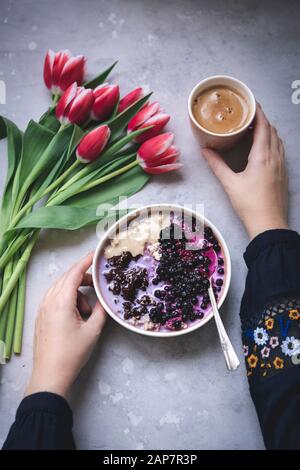 Woman having a bowl of porridge topped with melted chocolate, tahini and blueberries for breakfast Stock Photo