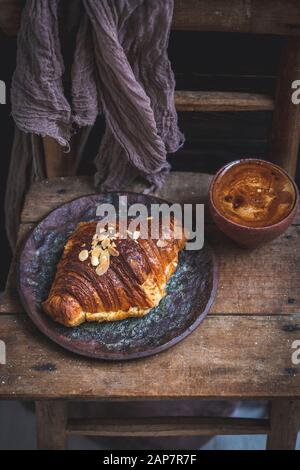 Almond croissant and cup of coffee served on an old rustic wooden chair Stock Photo