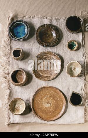 Variety of empty different handmade ceramic dishes, bowls, jugs and plates over grey linen cloth as background. Flat lay, space Stock Photo
