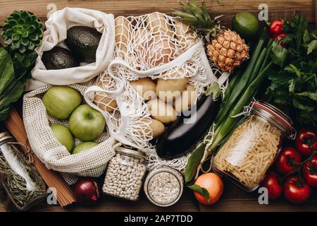 Zero waste food shopping. Fruit and vegetables in cotton bags, pasta, cereals and legumes in glass jars, herbs and spices on wooden background. Health Stock Photo