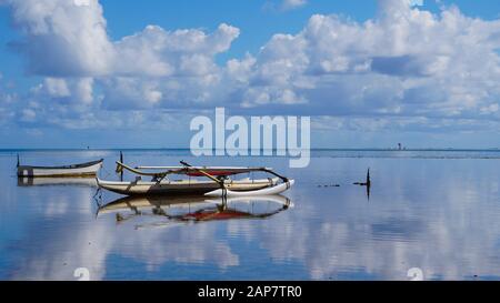 An outrigger canoe sits quietly on the mirror finished waters of Kaneohe Bay in Hawaii Stock Photo