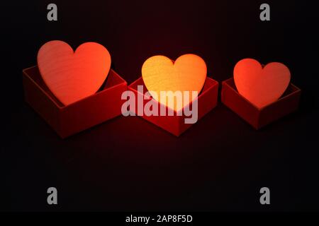 Three golden hearts in gift boxes on gray background. Red backlight Stock Photo