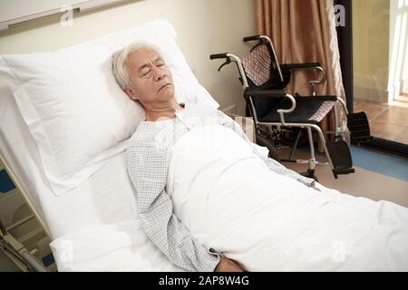 asian elderly male patient lying in bed sleeping in hospital ward or assisted living facility