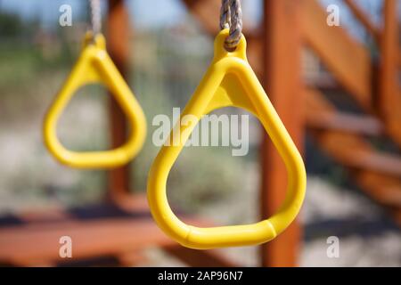 Yellow plastic rings on playground.Children play ground facility details.Kids swing on ropes and have fun outdoor in sunny summer day. Stock Photo