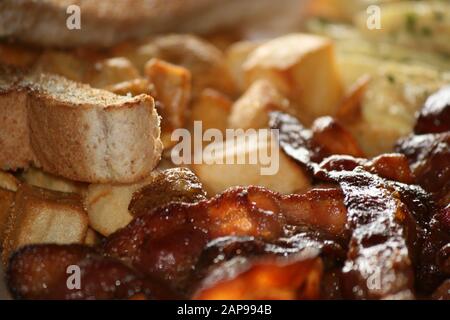 crispy well cooked pork bacon strips fried or grilled with hash browns and toast with tomato on plate in a close up view for breakfast lunch or dinner Stock Photo