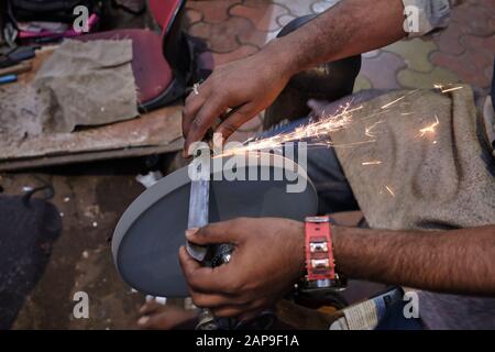 Sparks are flying off the whetstone of a knife sharpener at work  in Mumbai, India, propelled by a bicycle-like pedaling device Stock Photo