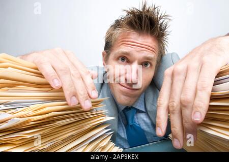 Office worker with huge pile of paperwork looking resigned to the work ahead of him Stock Photo