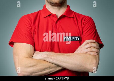 security service guard in red uniform standing on gray background with arms crossed Stock Photo