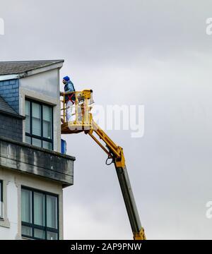 Coruna / Spain - January 22 2020: Man working repairing a apartment block using a self-propelled elevating work platform Stock Photo