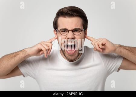 Head shot portrait millennial irritated man plugging fingers in ears. Stock Photo