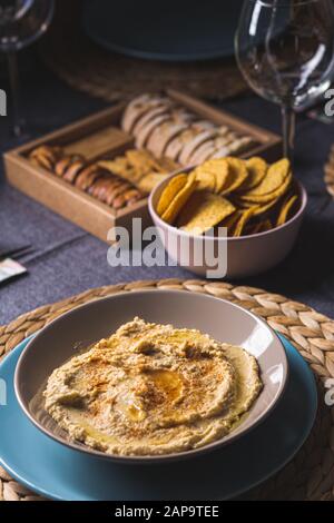 Tasty hummus chickpea food sauce on a plate on a blue and grey fabrics dinner table on a black background Stock Photo