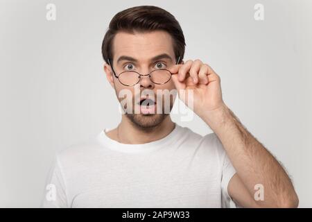 Young shocked surprised man looking at camera, taking off glasses. Stock Photo