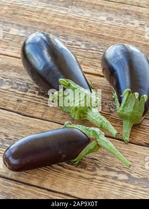 Just picked three eggplants on old wooden boards. Just harvested vegetables. Top view. Stock Photo
