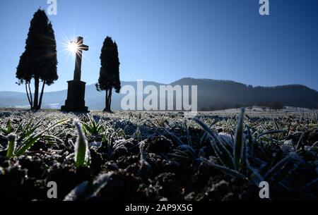 22 January 2020, Baden-Wuerttemberg, Hechingen: The sun is behind a wayside cross on a field with frost. Photo: Sebastian Gollnow/dpa Stock Photo