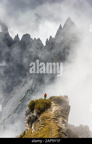 Mountaineer stands on a ridge, behind mountain peaks and pointed rocks, dramatic clouds, Cimon di Croda Liscia and Cadini Group, Auronzo di Cadore Stock Photo