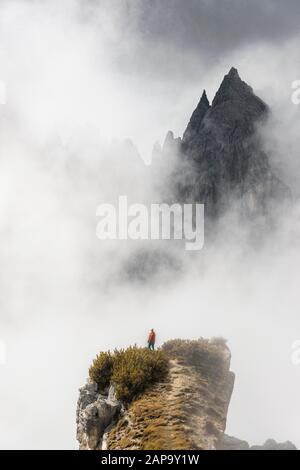 Mountaineer stands on a ridge, behind mountain peaks and pointed rocks, dramatic clouds, Cimon di Croda Liscia and Cadini Group, Auronzo di Cadore Stock Photo