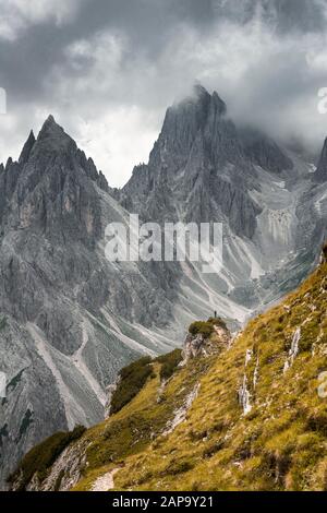 Mountaineer stands on a ridge, behind mountain peaks and pointed rocks, dramatic clouds, Cimon di Croda Liscia and Cadini Group, Auronzo di Cadore Stock Photo