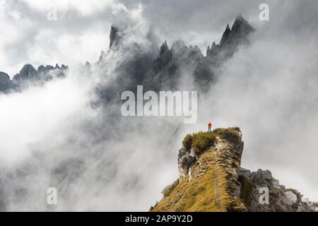 Mountaineer stands on a ridge, behind mountain peaks and pointed rocks, dramatic clouds, Cimon di Croda Liscia and Cadini Group, Auronzo di Cadore Stock Photo