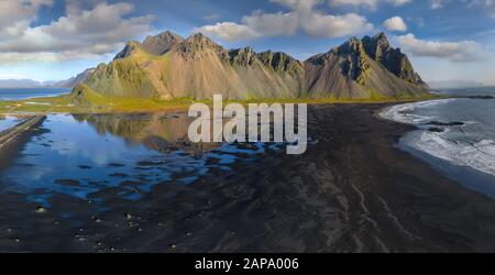 Epic aerial drone view flying over landscape of the black sand beach in Stokksnes on a sunny day. Vestrahorn mountain in the background. Nature and ec Stock Photo