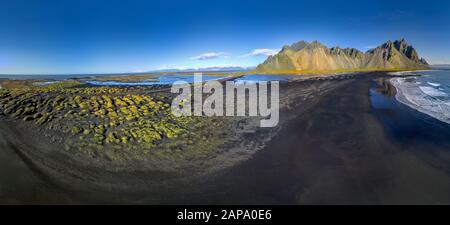 Epic aerial drone view flying over landscape of the black sand beach in Stokksnes on a sunny day. Vestrahorn mountain in the background. Nature and ec Stock Photo