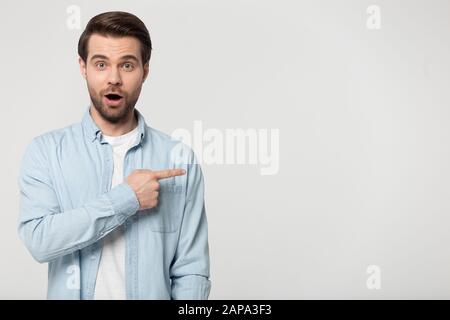 Excited young man standing aside, pointing at empty copy space. Stock Photo