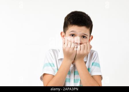 Cute scared little child boy in t-shirt looking at the camera on white background. Human emotions and facial expression Stock Photo