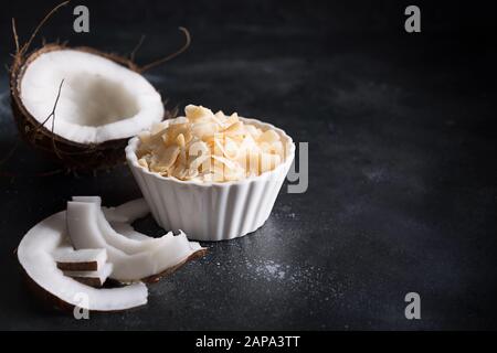 Organic Coconut Chips flakes in white bowl on black background. Copy space. Stock Photo