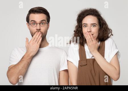 Surprised millennial joyful shy couple covering mouths with hands. Stock Photo