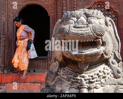 Rock carved sculpture of an demon in front of a temple, a woman stepping out of a door behind Stock Photo