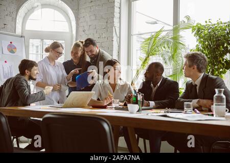Coffee break. Group of young business professionals having a meeting. Diverse group of coworkers discuss new decisions, plans, results, strategy. Creativity, workplace, business, finance, teamwork. Stock Photo