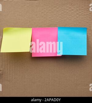blank square multicolored sheets of paper stickers glued on a brown cardboard surface Stock Photo