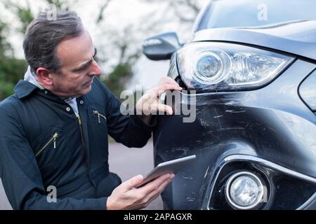 Auto Workshop Mechanic Inspecting Damage To Car And Filling In Repair Using Digital Tablet Stock Photo