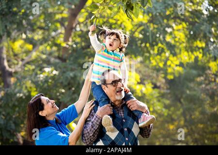 Grandmother with granddaughter sitting on grandfather's shoulder at park Stock Photo