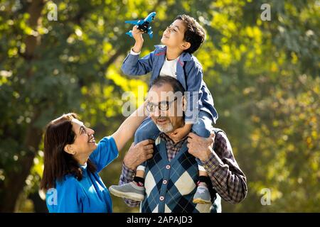 Grandmother with boy holding toy airplane sitting on grandfather's shoulder at park Stock Photo