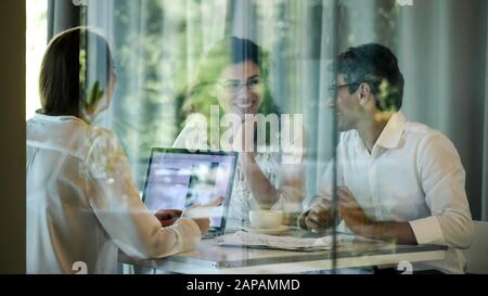 Businessmen sit at a table in a room behind a glass wall. Entrepreneurs are discussing a new project in the meeting room. Stock Photo