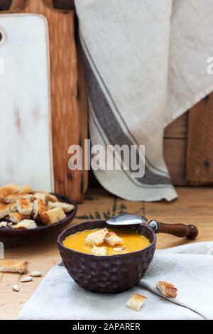 Vegetable soup puree of pumpkin, carrots and celery, served with croutons and pumpkin seeds. Rustic style. Stock Photo