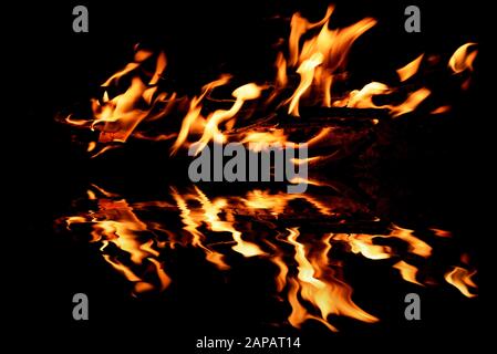 Beautiful bright flame from a fire on a black background with reflection in the water Stock Photo