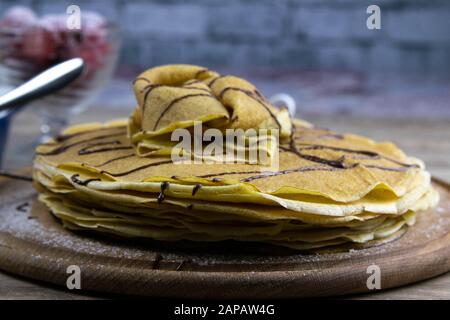 Pancakes with butter and chocolate on a wooden round board on the wooden background with chocolate, strawberry and seeds pours chocolate Stock Photo
