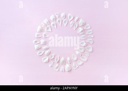 Round frame made of white rose petals on a pink wooden background. Flat lay, top view. Minimalistic floral background. Stock Photo