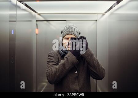 Male photographer taking a self picture in an elevator. Mirror selfie portrait, learning photography and analog film look concept. Stock Photo