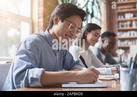 Young asian guy taking notes, having business meeting with colleagues Stock Photo