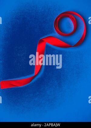 red silk ribbon twisted on a trendy classic blue background, festive postcard, copy space Stock Photo