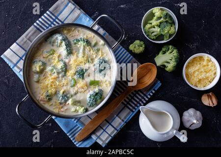 broccoli and cheddar cheese soup in a saucepot on a concrete table with grated cheese and fresh cream at the background, horizontal view from above, f Stock Photo