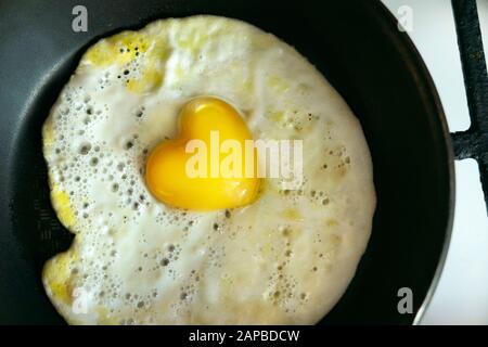 Fried egg heart shaped in pan for Valentines Day. Morning cooking food background. Heart of symbol love. Stock photo. Stock Photo
