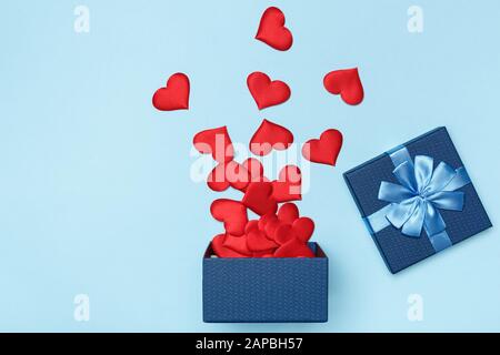 Scattered red hearts from a blue open gift box on a colored background. The concept of love and Valentine's Day. Stock Photo