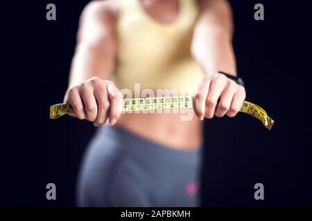 Woman with short blond hair in sport clothes holding measurement tape. Fitness, diet and healthcare concept Stock Photo