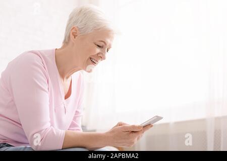 Positive retired lady using modern smartphone at home Stock Photo