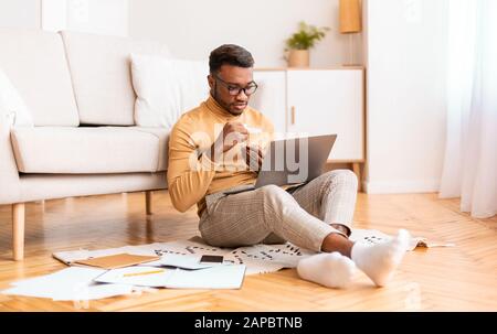 Afro Man Working On Laptop Having Coffee Sitting On Floor Stock Photo