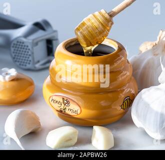 A close up view of a honey pot with a dipper dripping honey and surrounded by garlic and a garlic press. Stock Photo